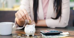 Close-up of woman dropping golden coin into white piggy bank