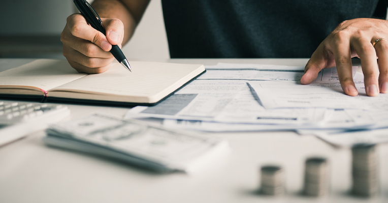 Man looking at bills while writing in a notebook with a pen