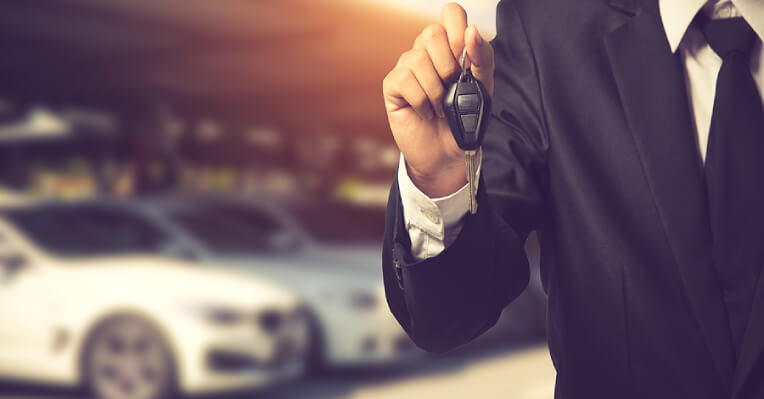 Close-up of man's hand holding car key with white car in background