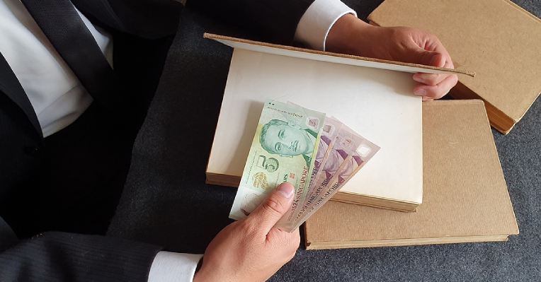 Close-up of man's hands putting Singapore $2 and $5 currency notes inside hardcover book