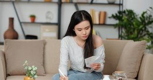 Young woman sitting on a couch looking at her bills and making notes