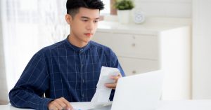 Young man typing on his laptop while holding his bills