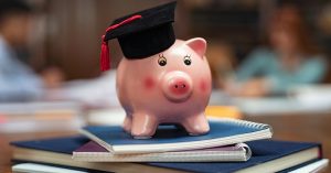 Pink ceramic pig figurine with a black graduate cap on top of notebooks