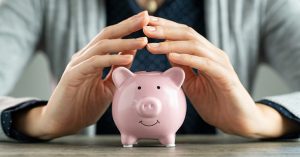 Woman's hands above a pink piggybank on a table