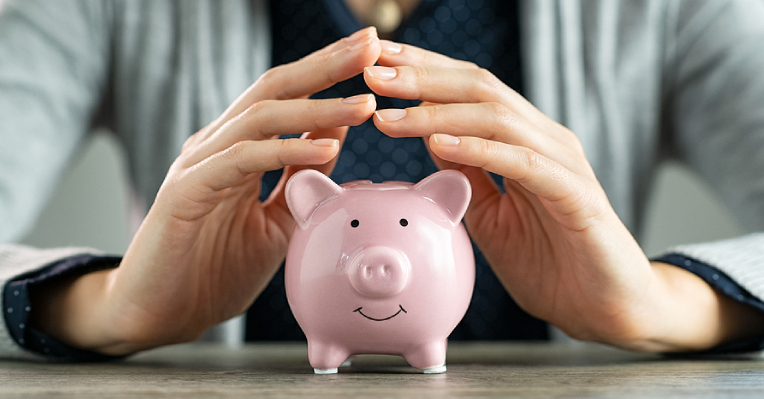 suggest to update to: Woman's hands above a pink piggybank on a table thinking of how to save and pay off her loan