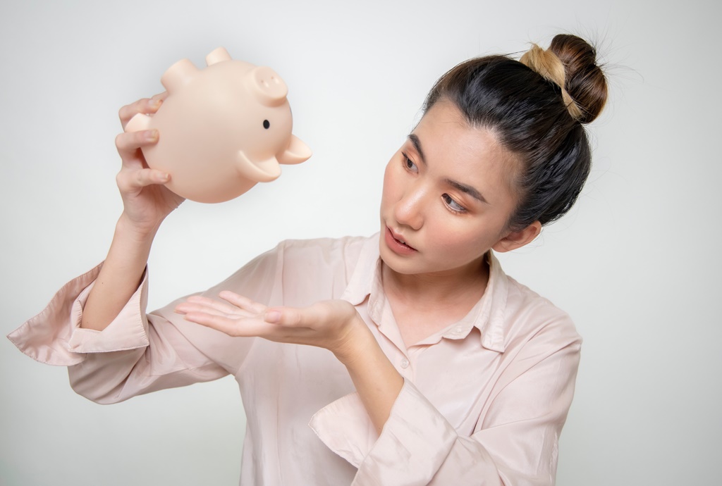 Asian woman looking at her piggy bank to illustrate the concept of getting an emergency payday loan with direct lender